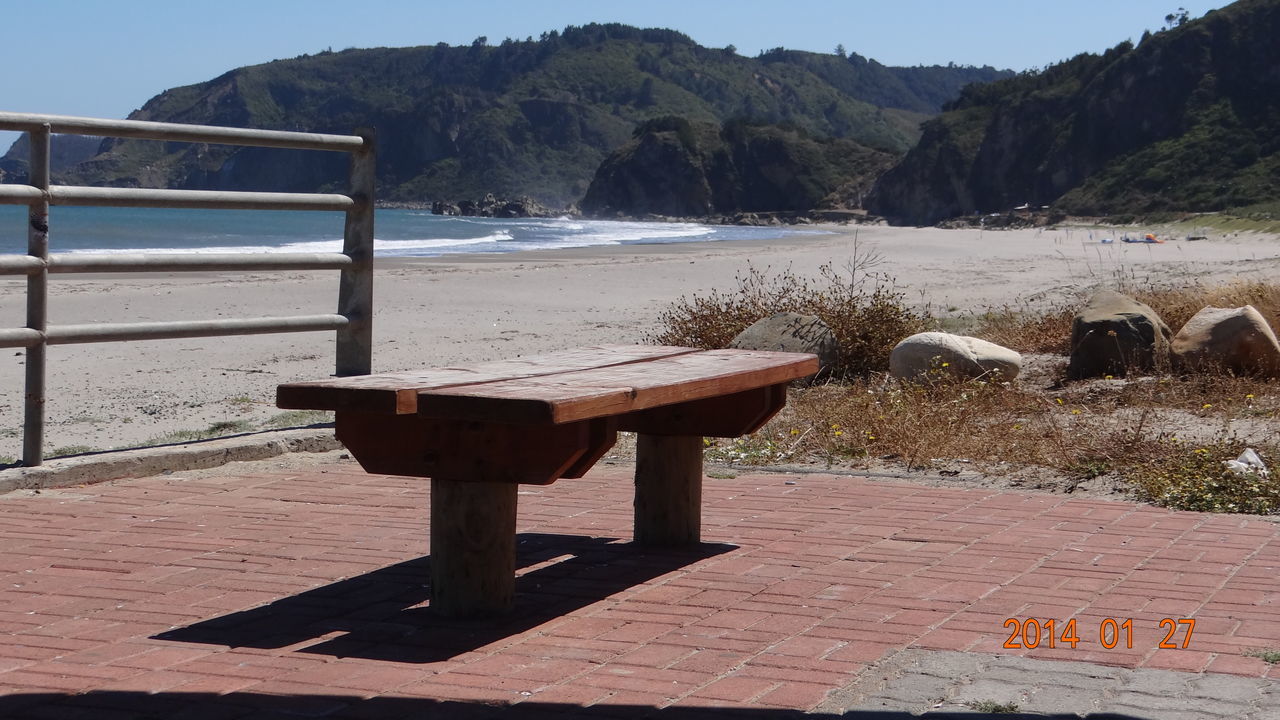 mountain, water, tranquility, tranquil scene, sunlight, bench, railing, nature, wood - material, scenics, lake, pier, outdoors, empty, shadow, beauty in nature, day, tree, beach, mountain range