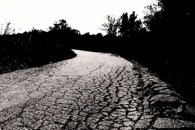 Road amidst silhouette trees on landscape