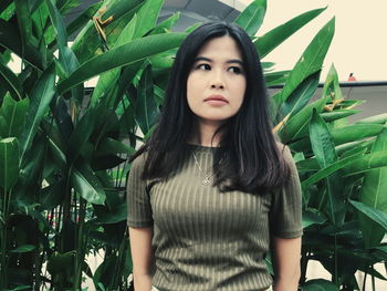 Portrait of beautiful young woman standing against plants