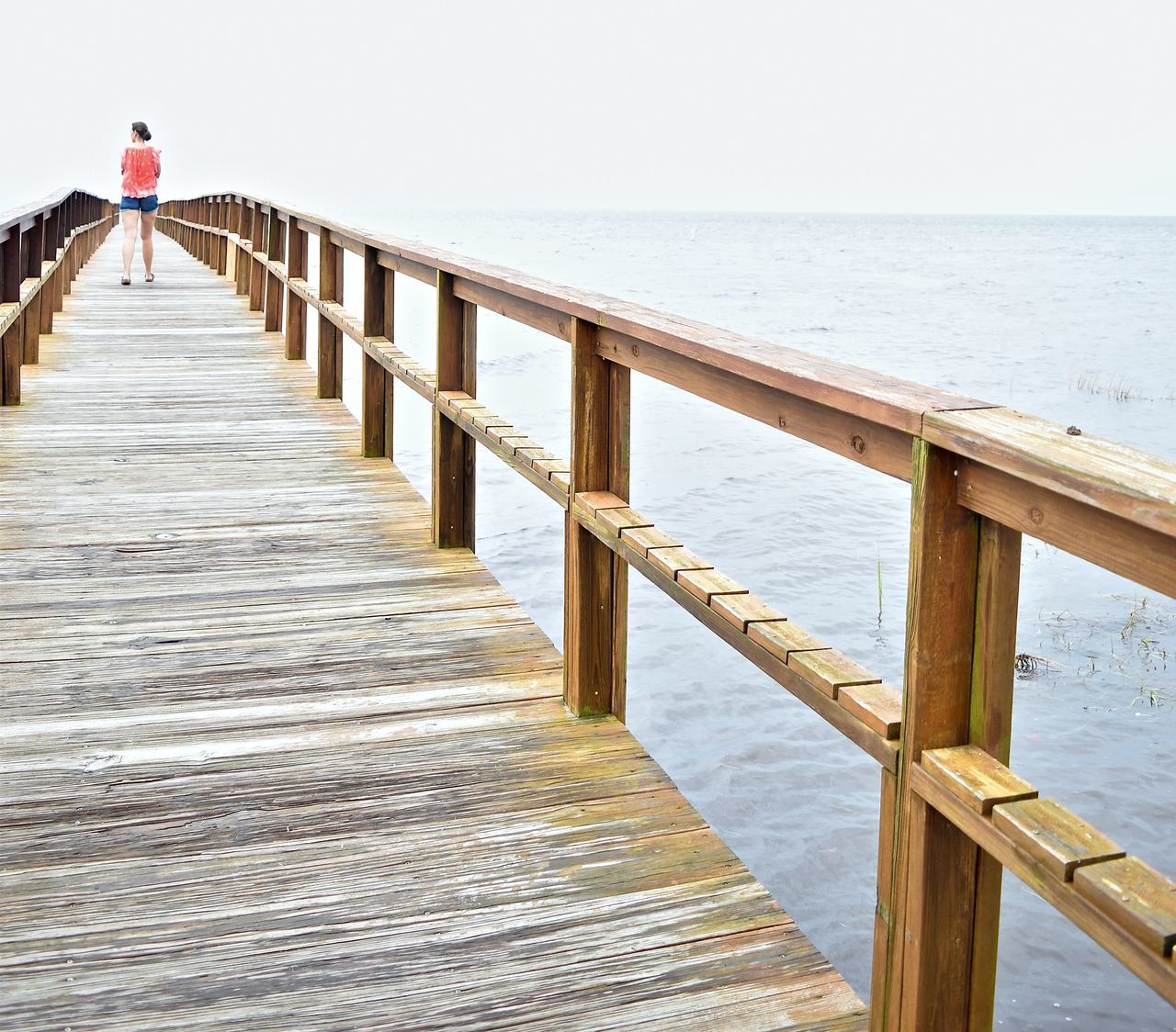 MAN STANDING ON PIER BY SEA AGAINST SKY