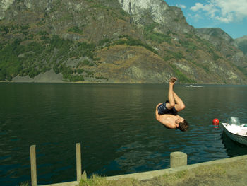 Shirtless man diving in lake by mountain