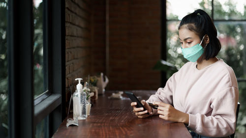 Young woman using smart phone on table at window