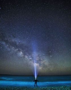 Rear view of man with headlamp standing on shore at beach against sky at night