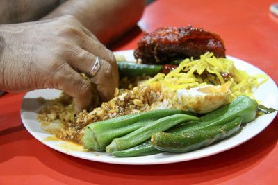 Cropped hand of man having food in plate on table