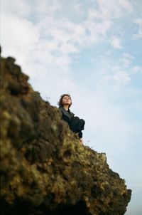 Low angle view of woman sitting on rock against sky