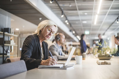 Senior female entrepreneur writing in diary while working at table in office