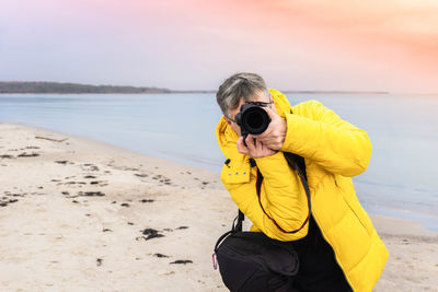 Man photographing with yellow umbrella on beach