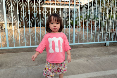 Portrait of girl standing against metallic gate 