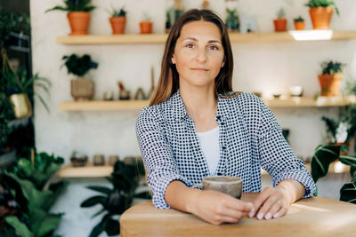 Attractive brunette woman 40s at the bar in a cozy shop with plants