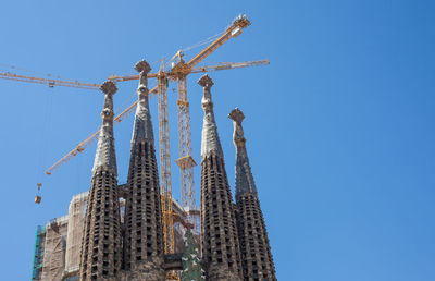 Low angle view of crane by building against clear blue sky