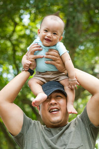 Father carrying son on head against tree