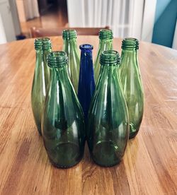 Colored glass bottle huddled in group, green blue wood table top high angle muted colors still life