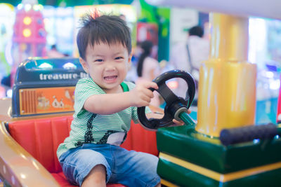 Portrait of smiling boy sitting in toy car at shopping mall