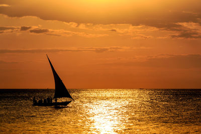 Silhouette sailboat sailing on sea against dramatic sky during sunset