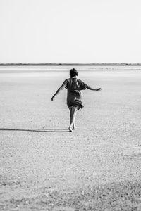 Rear view of woman walking at beach against clear sky