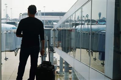 Rear view of man standing on glass window at airport