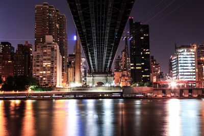 Illuminated buildings by river against sky in city at night