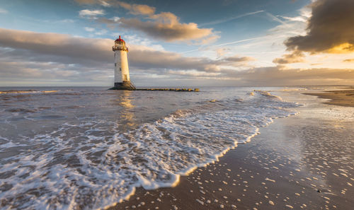 Lighthouse by sea against sky during sunset