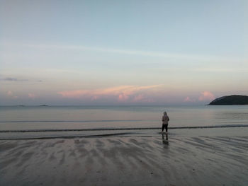 Man standing on beach against sky during sunset