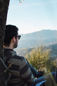 Side view of young man looking at mountain against sky
