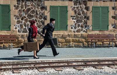 Full length of people with suitcase walking on railroad station platform