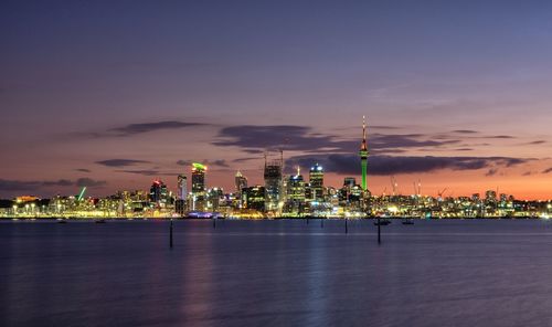 Illuminated city by sea against sky at night