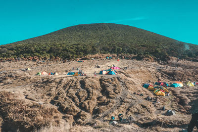 People on rocks by tents against mountain and sky