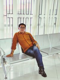 Portrait of man sitting on chair against tiled floor