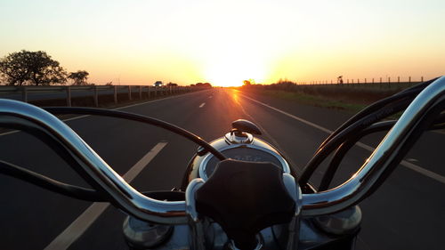 Rear view of man riding motorcycle on road against sky during sunset