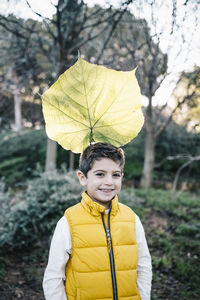 Portrait of smiling boy with leaf against trees