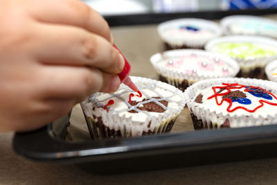 A child squeezes colored frosting from a tube onto chocolate brown cupcakes covered white frosting.