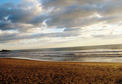 View of calm beach against cloudy sky