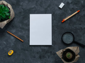 White blank notebook mockup dark background flat lay. minimal work space sketchbook pen green plant 