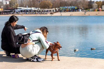 Young girl and her mother on relaxing vacation by the lake with their cute miniature pinscher.