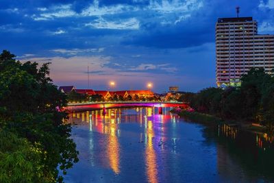 Illuminated buildings by river against sky in city