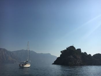 Boat moving on river by rock formation against clear blue sky