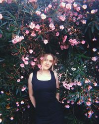 Portrait of young woman standing by flowering tree