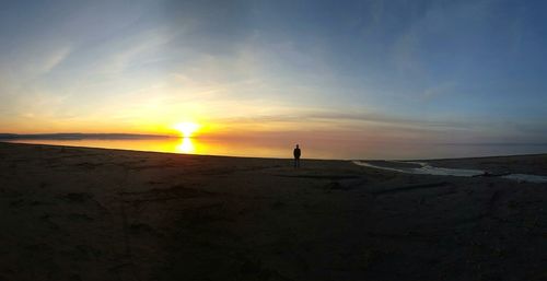 Distant view of man on beach against sky during sunset