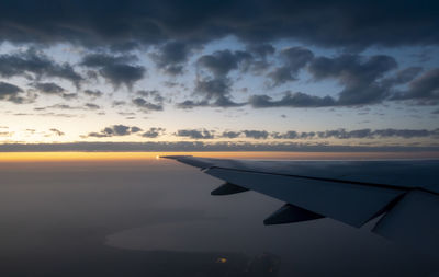 Airplane flying over sea against sky during sunset