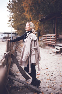 Thoughtful woman holding coat while standing by fence during winter