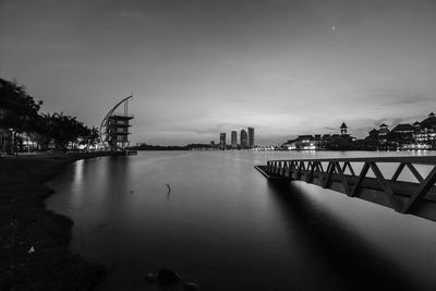 Bridge over river by buildings against sky at dusk