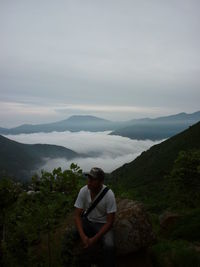 High angle view of young man sitting on rock against sky