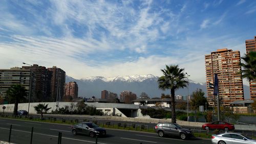 Cars on road by buildings in city against sky