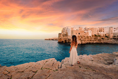 Rear view of woman by sea against sky during sunset