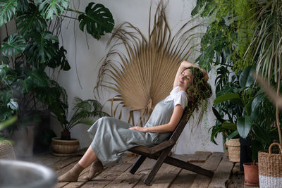 Dreamy woman relaxing in tropical resort-style garden at home, female gardener resting in greenhouse