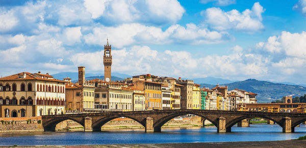 Bridge over river by buildings against sky in city