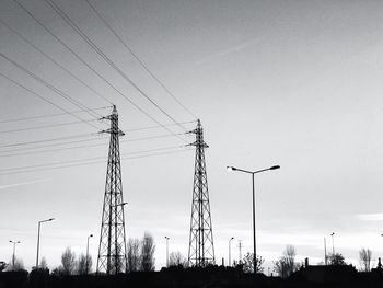 Low angle view of silhouette electricity pylons against sky