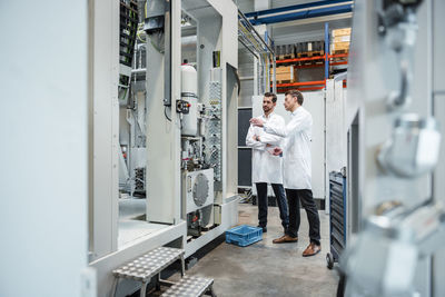 Two men wearing lab coats talking in factory