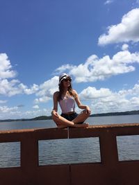 Tilt shot of smiling woman sitting on railing against sky