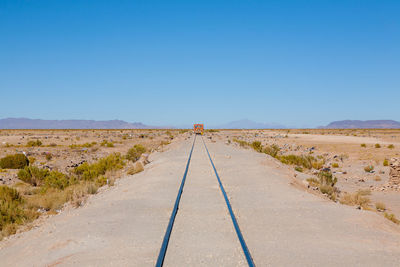 Road leading towards desert against clear blue sky